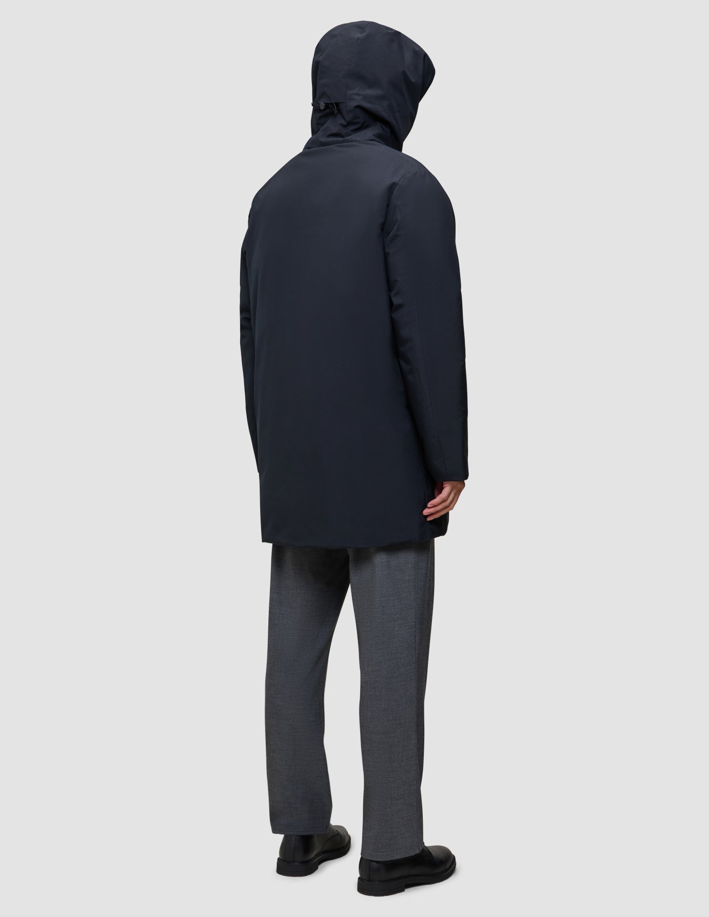 En person set bagfra, iført en sort Utility Jacket, grå bukser og sorte sko.